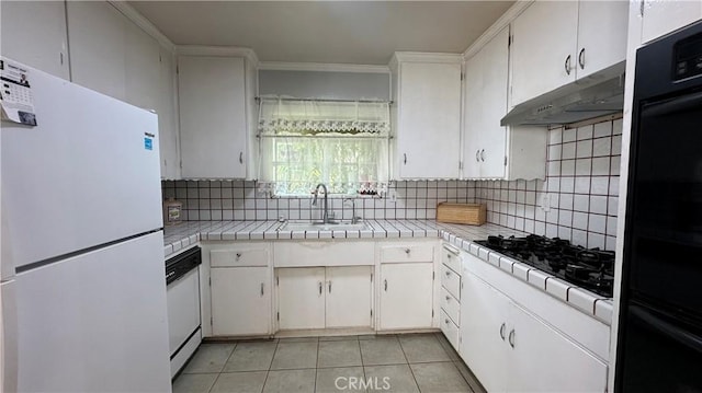 kitchen featuring tile counters, under cabinet range hood, decorative backsplash, black appliances, and a sink