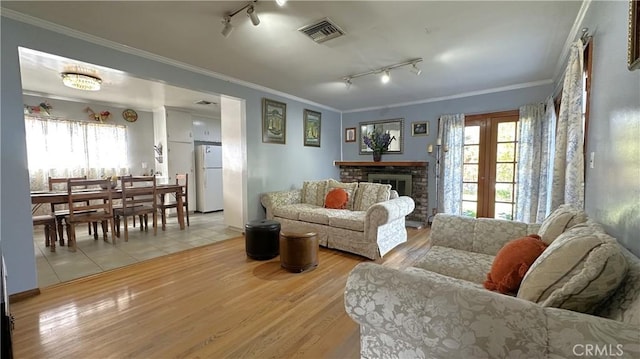 living room with a wealth of natural light, visible vents, light wood-type flooring, and crown molding