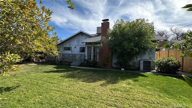 exterior space featuring central AC unit, fence, a yard, stucco siding, and a chimney