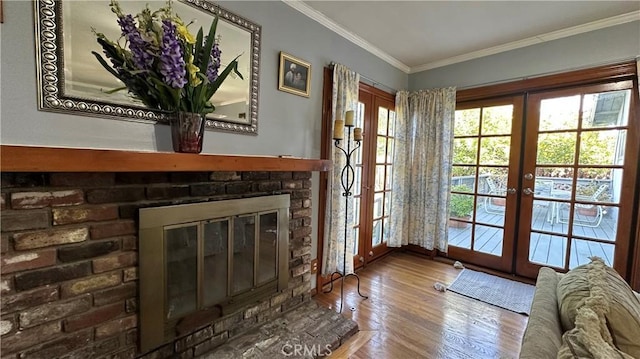 doorway to outside with crown molding, a brick fireplace, wood finished floors, and french doors