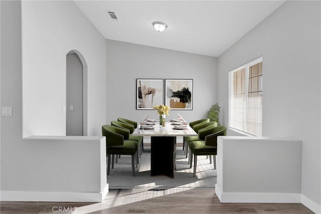 dining room featuring wood finished floors, baseboards, visible vents, lofted ceiling, and arched walkways