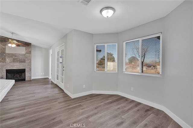 unfurnished living room with visible vents, baseboards, wood finished floors, and a tiled fireplace