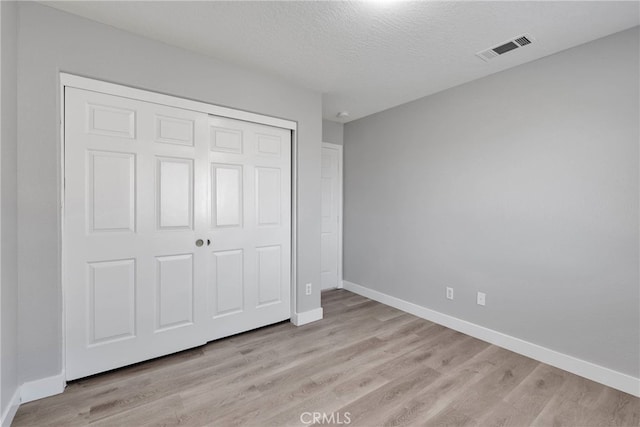 unfurnished bedroom with baseboards, visible vents, light wood-style flooring, a closet, and a textured ceiling