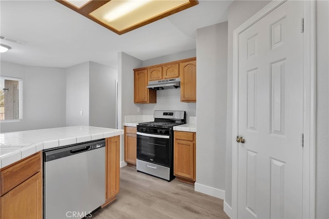 kitchen with visible vents, under cabinet range hood, tile countertops, light wood-style flooring, and appliances with stainless steel finishes