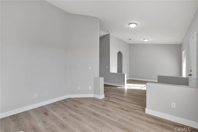 empty room featuring baseboards, arched walkways, and light wood-style flooring