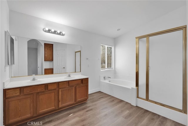 full bathroom featuring a shower stall, double vanity, wood finished floors, a bath, and a sink