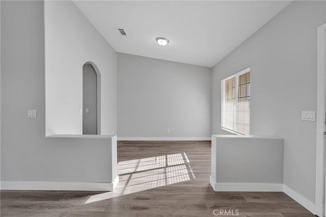 spare room featuring visible vents, baseboards, arched walkways, and wood finished floors