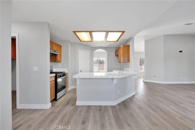 kitchen featuring tile countertops, light wood-type flooring, gas range, and under cabinet range hood