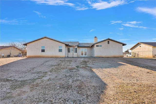 back of property with french doors, fence, a chimney, and stucco siding