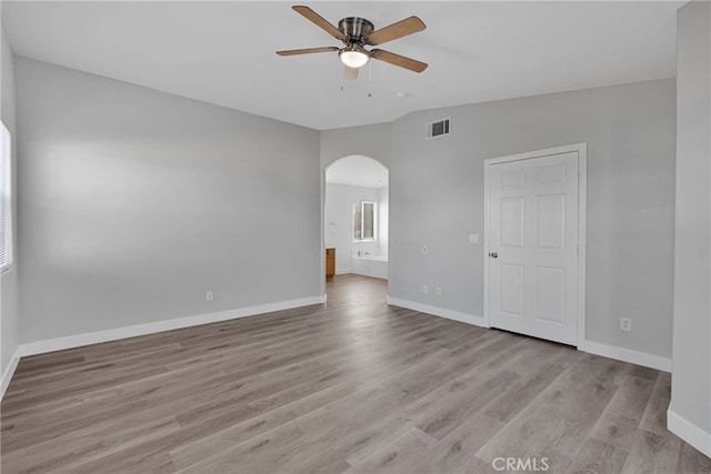 unfurnished room with a ceiling fan, visible vents, lofted ceiling, light wood-style flooring, and arched walkways