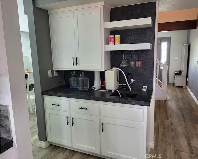 kitchen featuring a sink, dark countertops, white cabinetry, decorative backsplash, and wood tiled floor