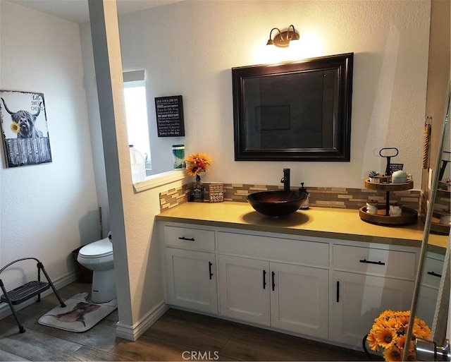 bathroom featuring baseboards, tasteful backsplash, toilet, and vanity