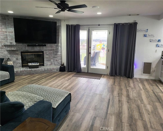 living room featuring a ceiling fan, a brick fireplace, wood finished floors, and visible vents