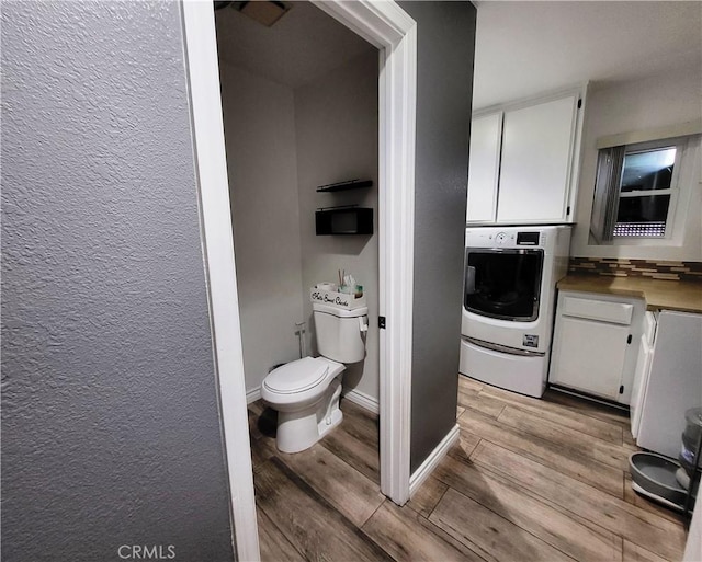 bathroom featuring baseboards, washer / clothes dryer, toilet, and wood finished floors