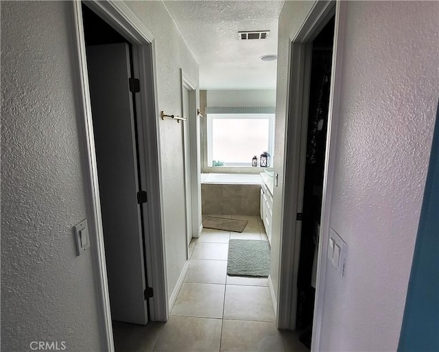 hall with light tile patterned floors, baseboards, visible vents, a textured ceiling, and a textured wall