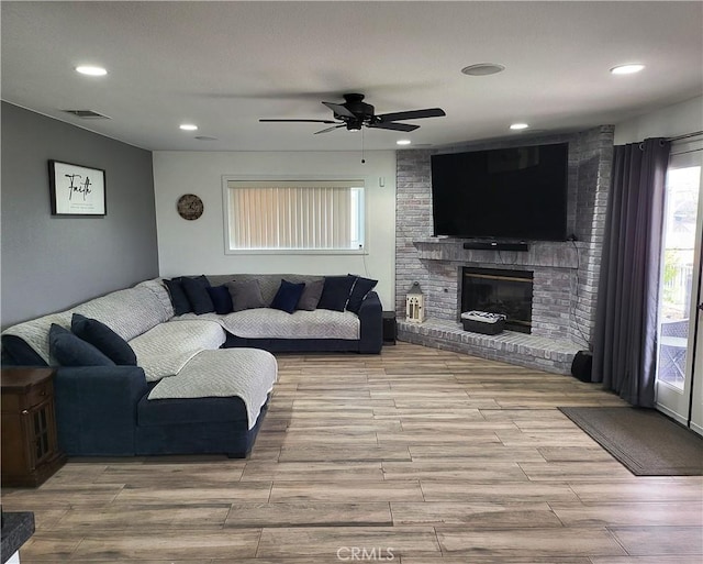 living room with a brick fireplace, wood finished floors, visible vents, and ceiling fan