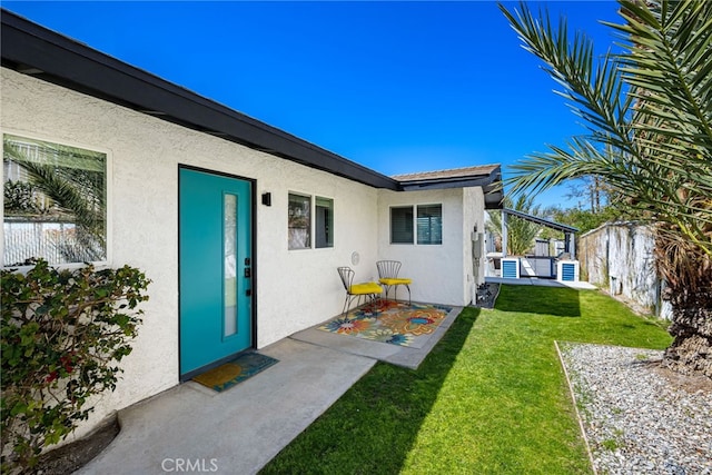 doorway to property featuring a yard, stucco siding, and fence