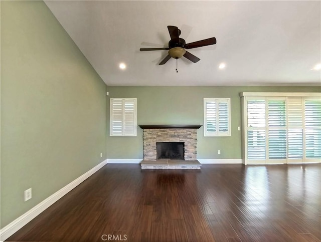 unfurnished living room with dark wood-style floors, a stone fireplace, ceiling fan, and baseboards