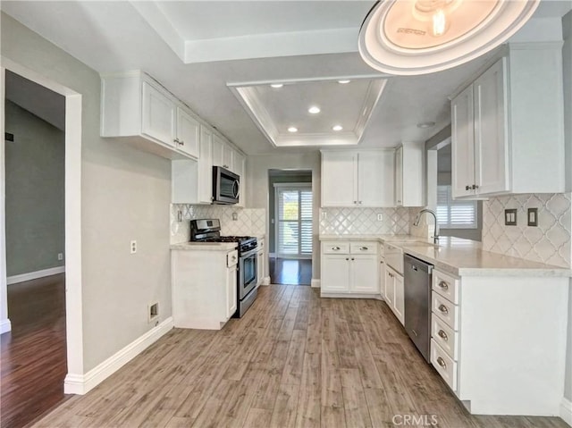 kitchen featuring light wood-type flooring, a tray ceiling, light countertops, white cabinets, and stainless steel appliances