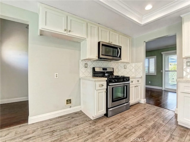 kitchen featuring light wood-style flooring, a tray ceiling, tasteful backsplash, appliances with stainless steel finishes, and light countertops