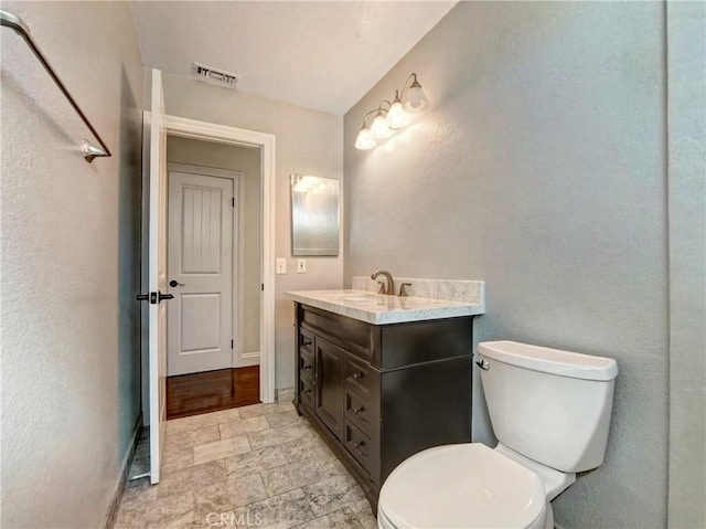 bathroom with visible vents, baseboards, toilet, stone finish floor, and vanity