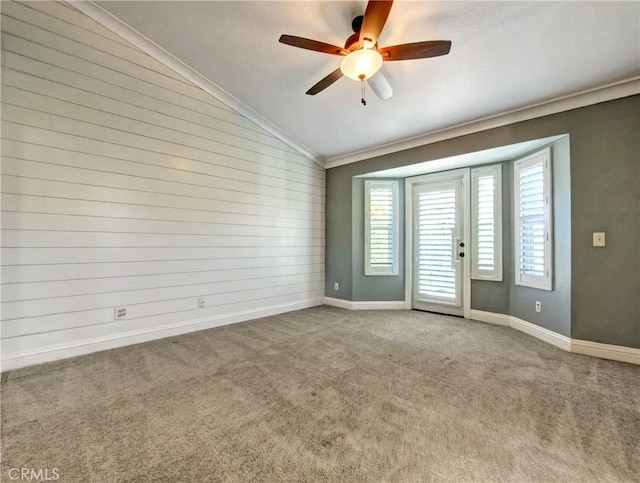 empty room with a ceiling fan, baseboards, carpet floors, vaulted ceiling, and crown molding