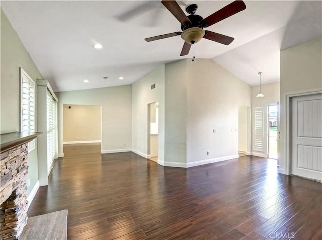 unfurnished living room with a stone fireplace, vaulted ceiling, dark wood-style floors, and baseboards