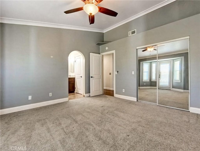 unfurnished bedroom with arched walkways, visible vents, ornamental molding, and carpet floors