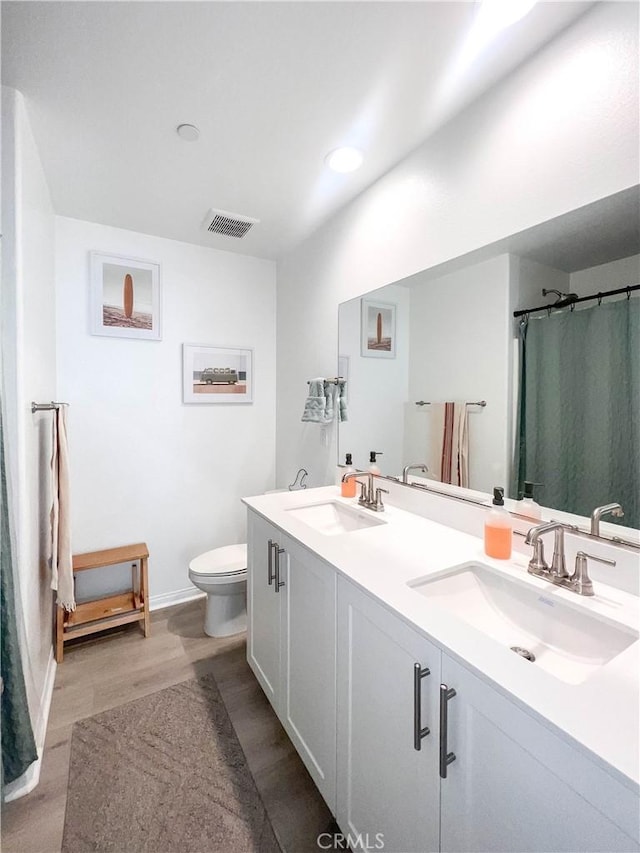 bathroom featuring toilet, wood finished floors, visible vents, and a sink