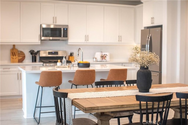 kitchen with a center island with sink, white cabinetry, stainless steel appliances, and light countertops