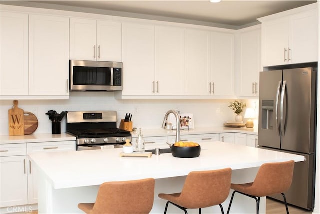 kitchen featuring a kitchen island with sink, stainless steel appliances, a breakfast bar area, and light countertops