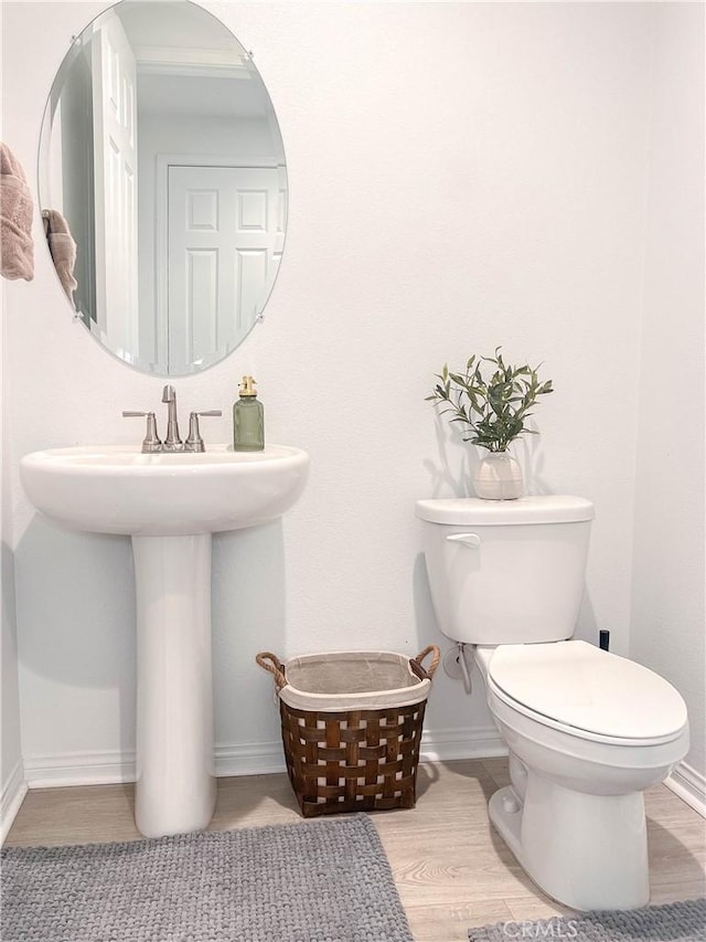 bathroom featuring toilet, wood finished floors, baseboards, and a sink