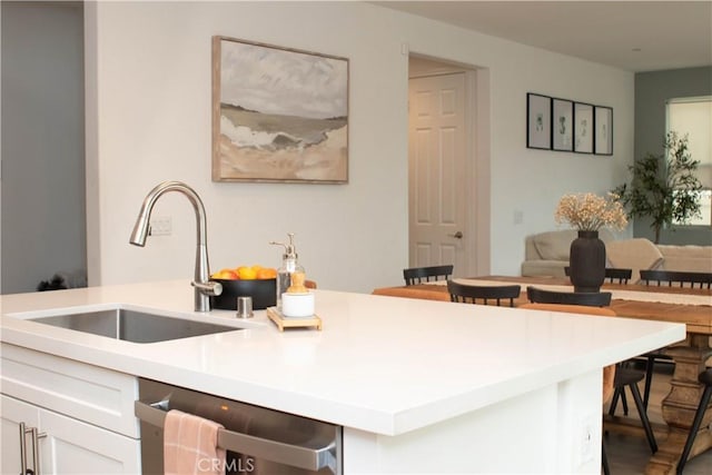 kitchen with light countertops, dishwashing machine, a kitchen breakfast bar, white cabinets, and a sink