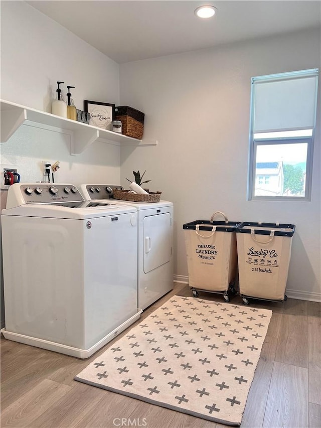 clothes washing area featuring baseboards, washing machine and dryer, laundry area, and light wood finished floors