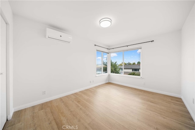 unfurnished room featuring baseboards, light wood-type flooring, and a wall mounted AC