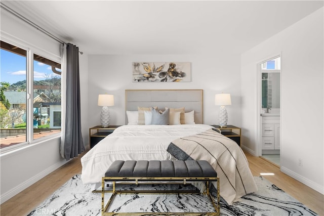 bedroom with connected bathroom, baseboards, and light wood-style floors