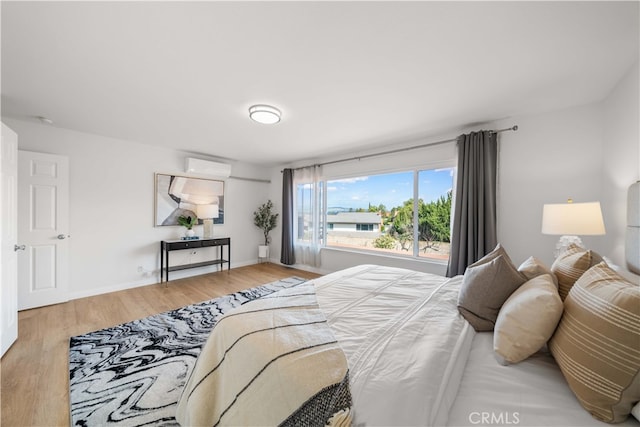 bedroom with an AC wall unit, wood finished floors, and baseboards