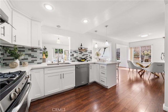 kitchen with dark wood finished floors, light countertops, appliances with stainless steel finishes, a peninsula, and a sink