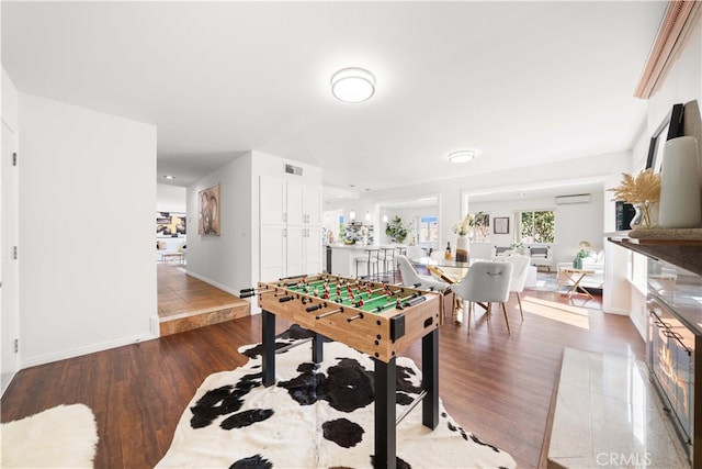 rec room featuring wood finished floors, visible vents, a wall mounted air conditioner, and baseboards