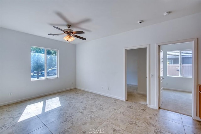 empty room with light tile patterned floors, a ceiling fan, and baseboards