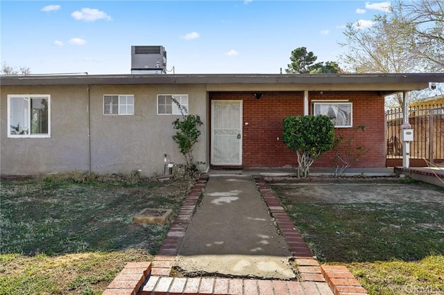 doorway to property with cooling unit, fence, brick siding, and stucco siding