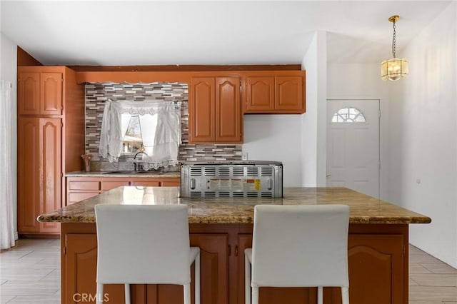 kitchen with light stone counters, backsplash, a center island, and a sink