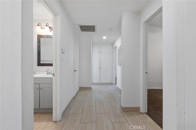 hall featuring a sink, visible vents, baseboards, and wood tiled floor