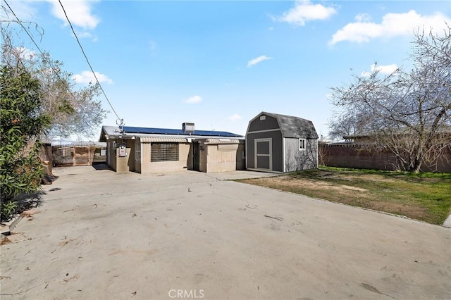 rear view of property featuring an outbuilding, a fenced backyard, a storage shed, a patio area, and roof mounted solar panels