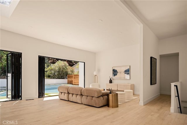 living room featuring a skylight, light wood-style floors, and baseboards