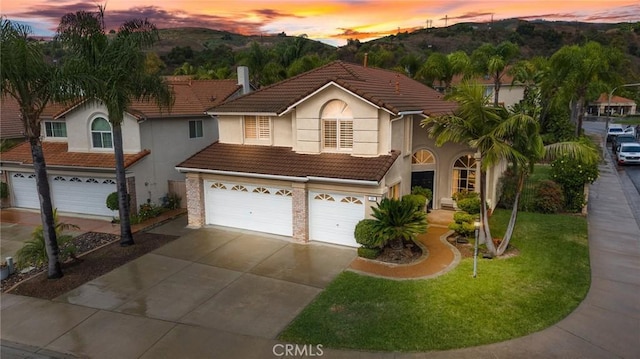 view of front of house with an attached garage, stucco siding, concrete driveway, a tile roof, and brick siding