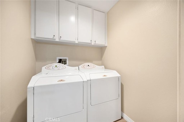 clothes washing area with washer and clothes dryer, cabinet space, and baseboards