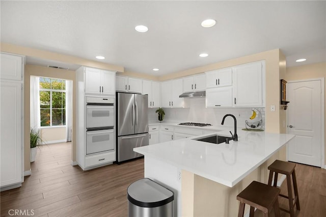 kitchen featuring gas cooktop, a peninsula, freestanding refrigerator, a sink, and under cabinet range hood