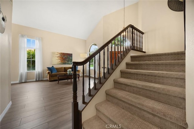 staircase featuring baseboards, high vaulted ceiling, and wood finished floors