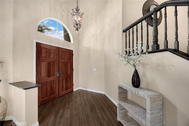 foyer with a notable chandelier, dark wood-style floors, baseboards, a towering ceiling, and stairs